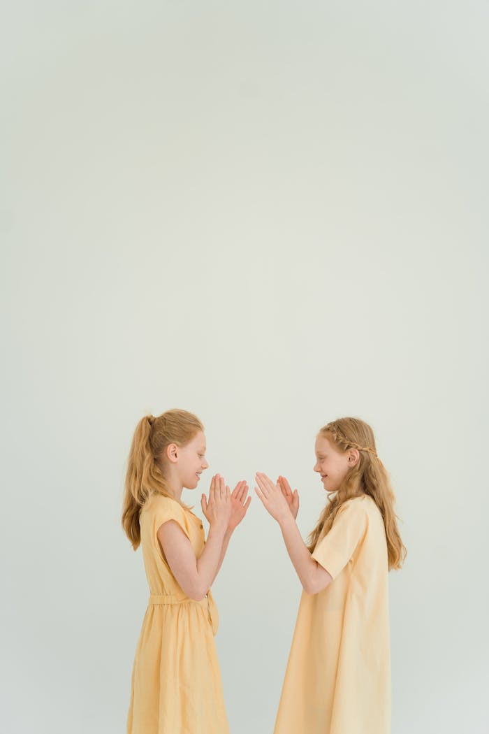 Twin girls in yellow dresses playing a handclap game indoors, capturing the joy of childhood.